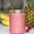 A refreshing pink smoothie made with bananas, raspberries, and tropical fruits in a glass jar.